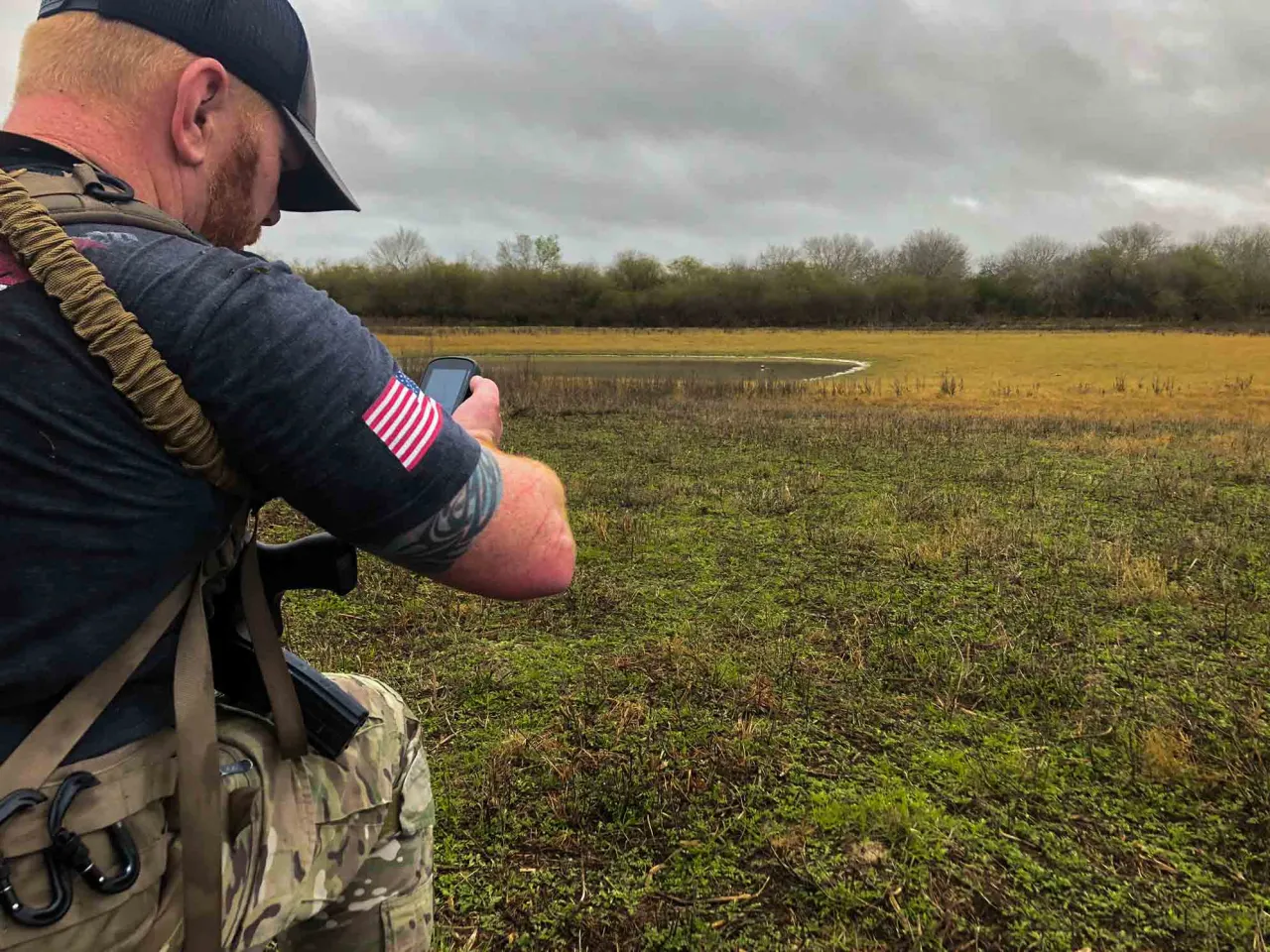 Student checking a phone ballistics app while kneeling at the edge of an open field range