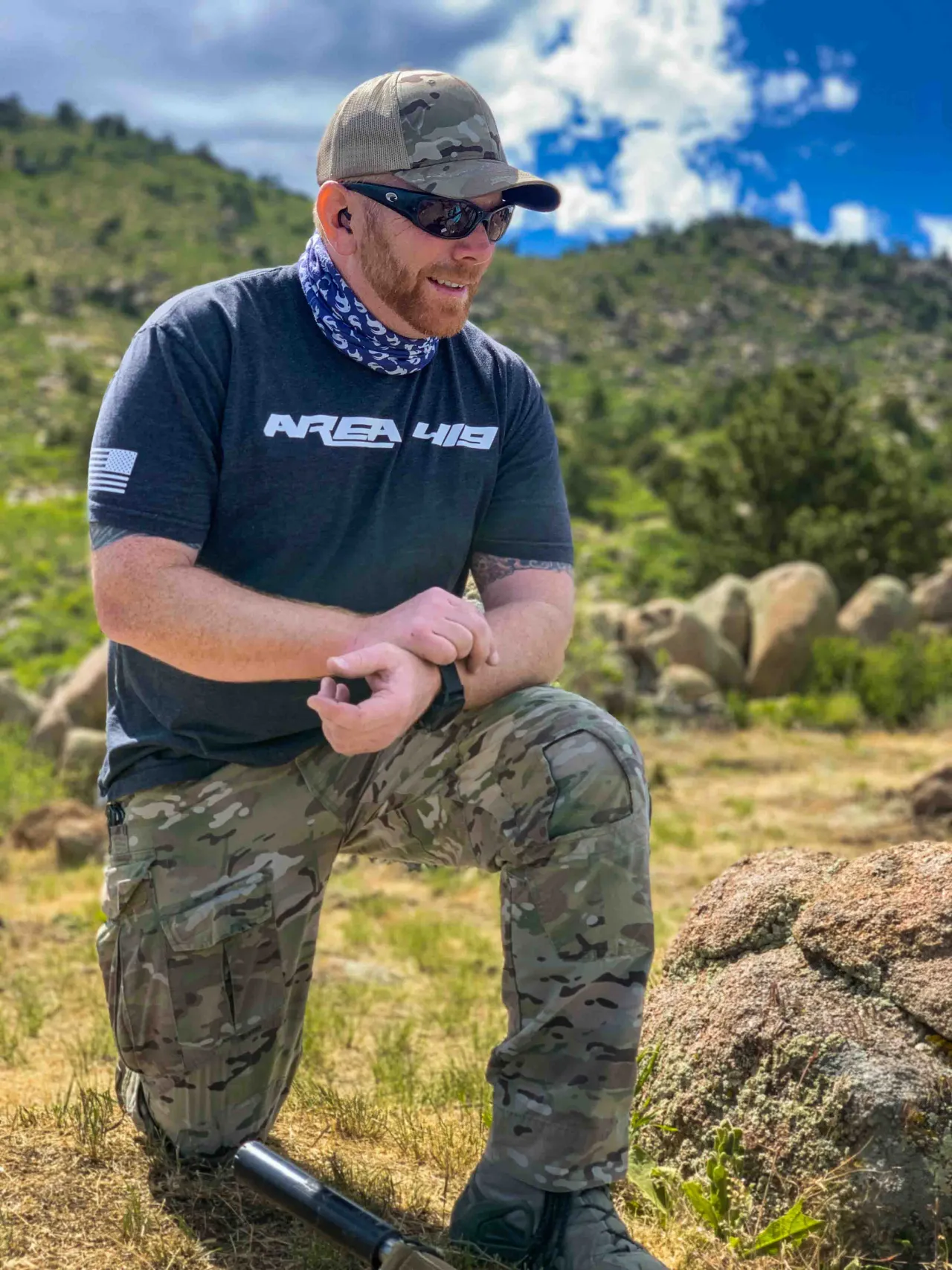 Instructor kneeling in the mountains, checking a wrist-mounted ballistic calculator