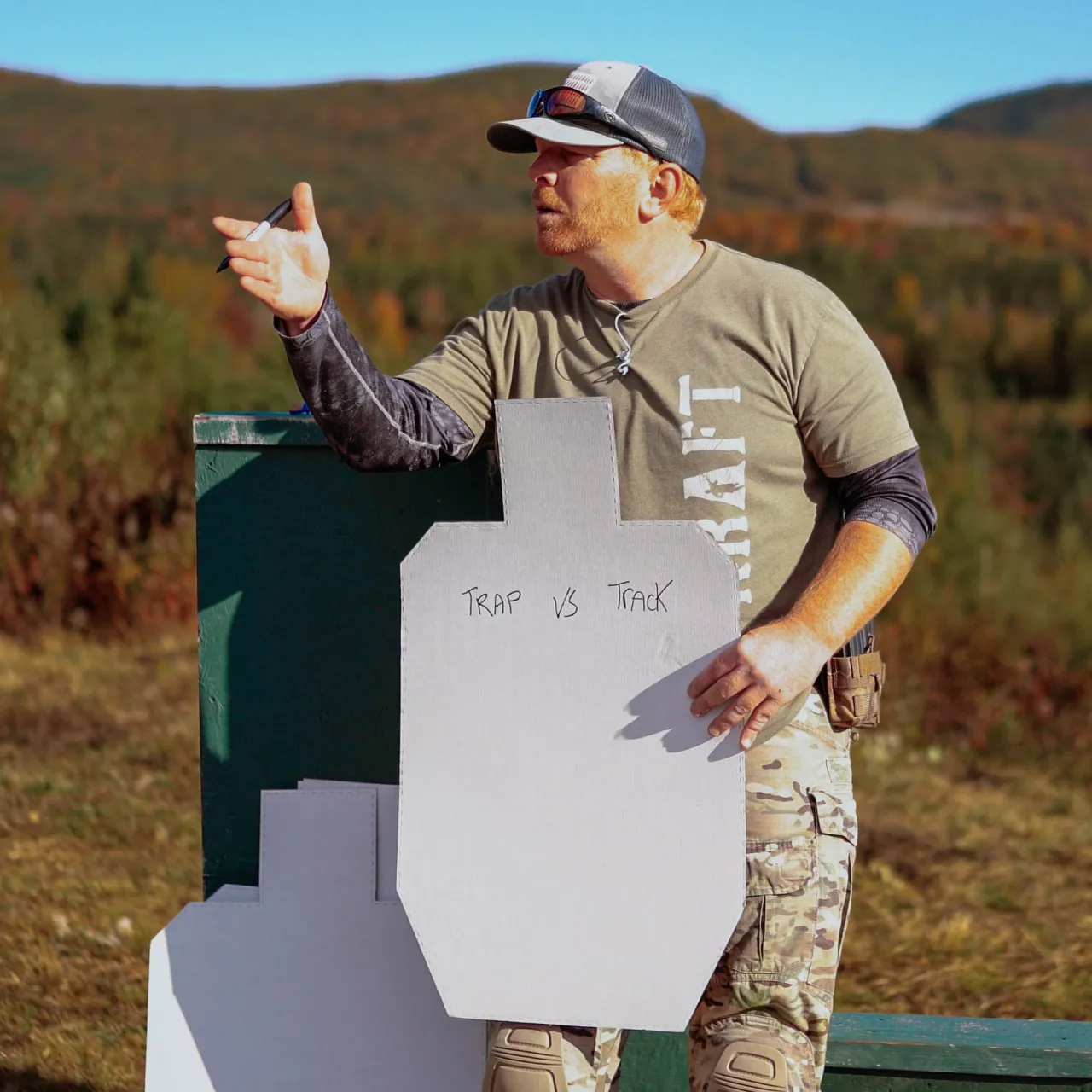 Instructor pointing to a cardboard target marked "Trap vs Track" while teaching