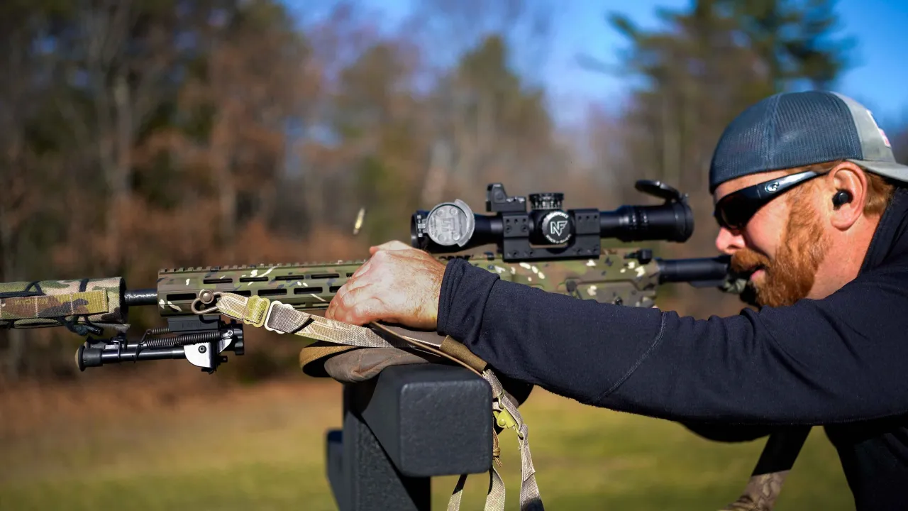 Shooter firing a rifle rested on a barricade, spent brass in the air