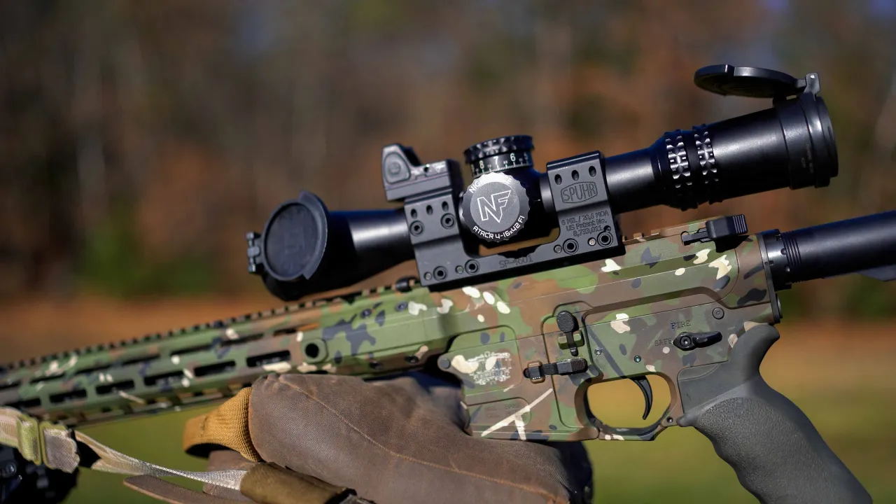 Close-up of a camouflage-finished precision AR rifle with a Nightforce scope, rested on a shooting bag