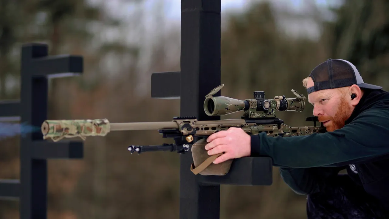 Shooter firing a suppressed rifle braced against a black barricade post