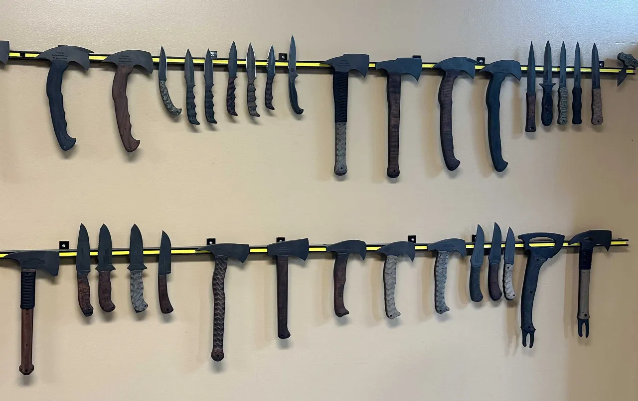 Wall display of training knives, hatchets and tomahawks on magnetic strips