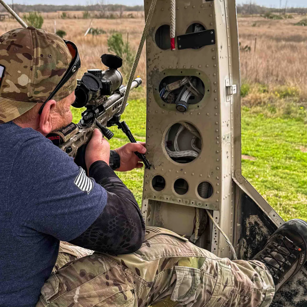 Shooter aiming a scoped rifle from inside a helicopter doorway mockup