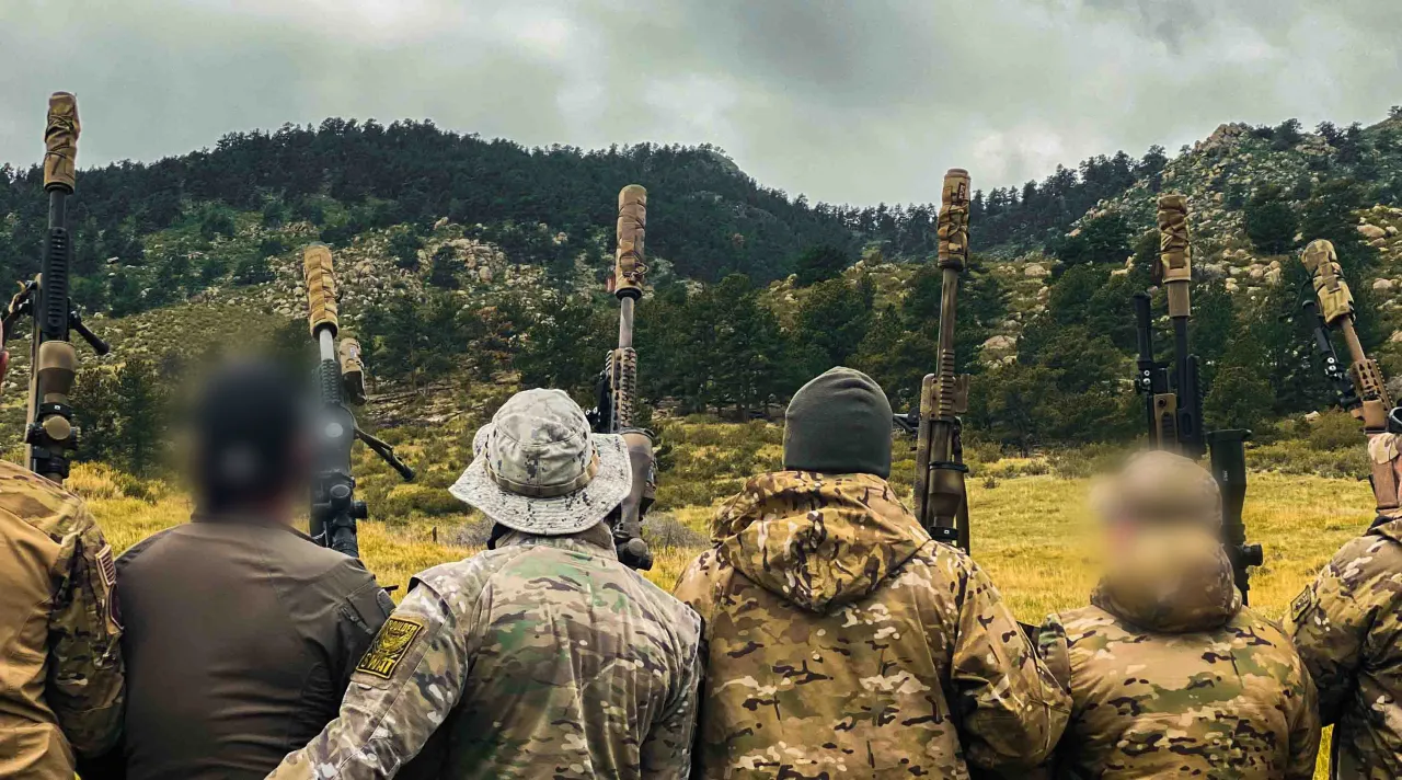 Students with rifles on their packs looking out over a mountain valley