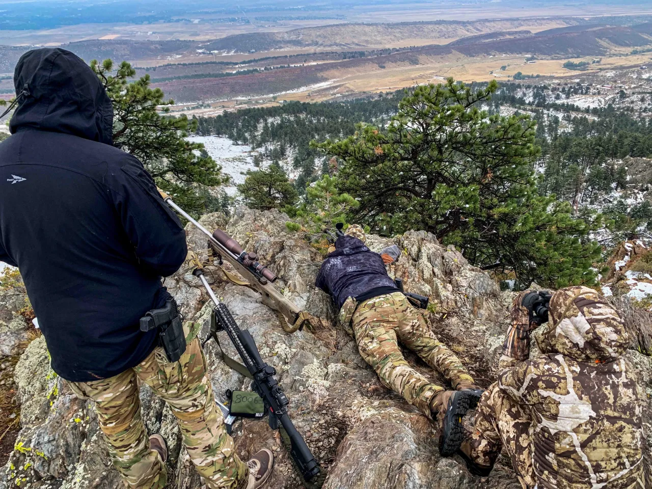 Students in the prone and standing on a rocky ridge overlooking a snowy valley
