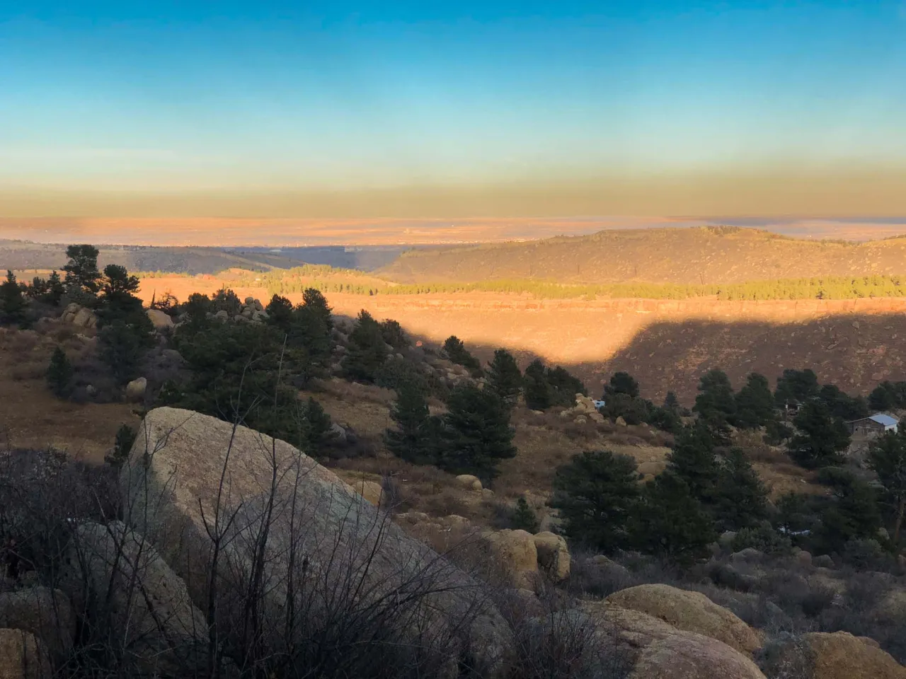 Golden morning light over rocky, pine-dotted foothills and the plains beyond