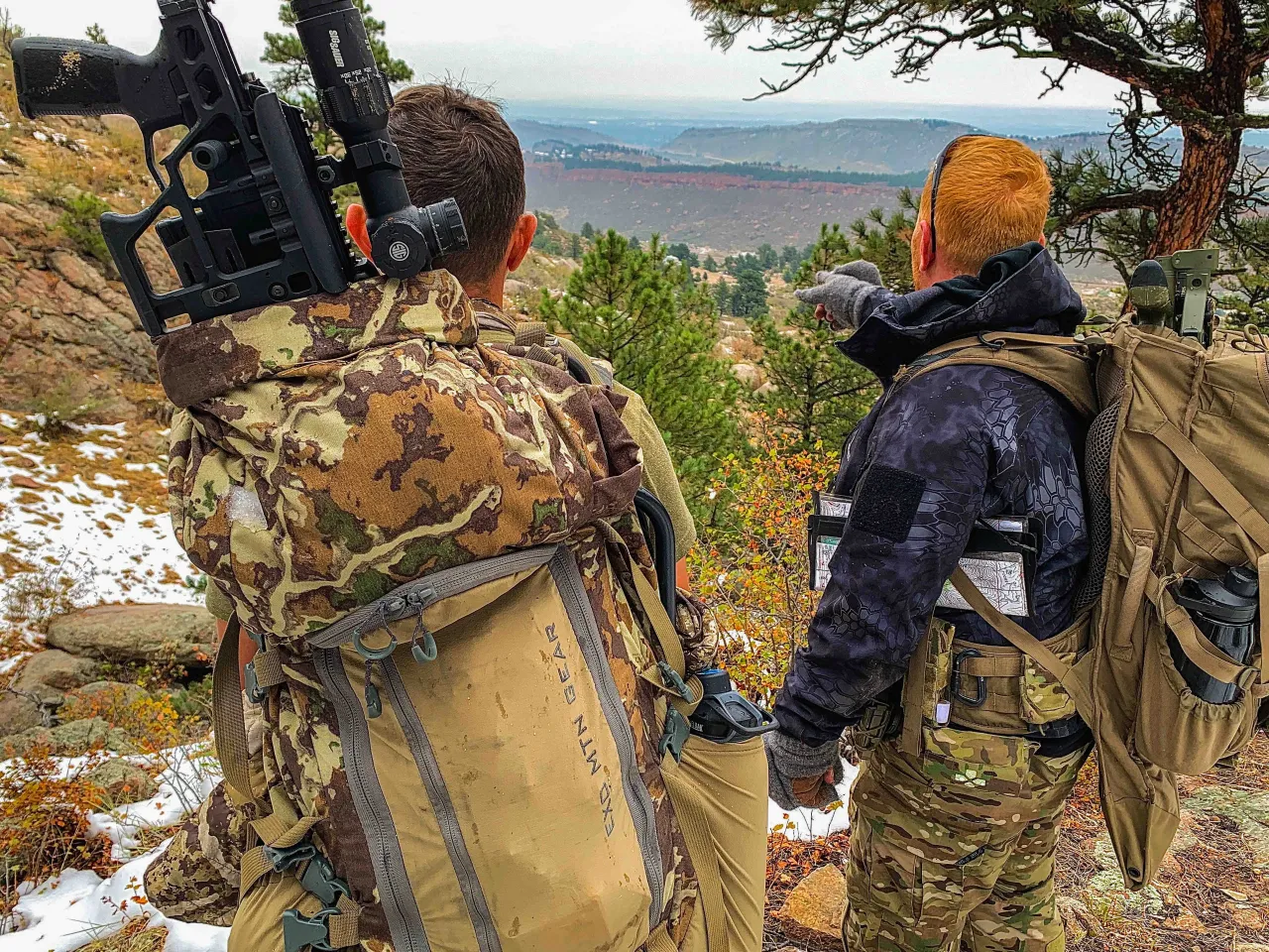 Two students with rifles on their packs, one pointing out a target across the valley
