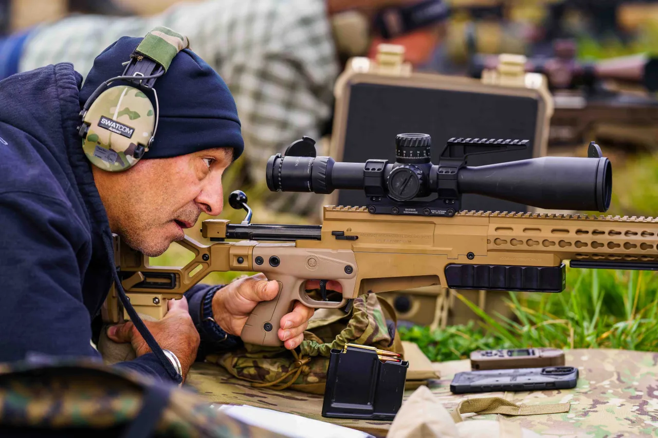 Instructor wearing hearing protection studying a tan chassis rifle with a large scope on the firing line