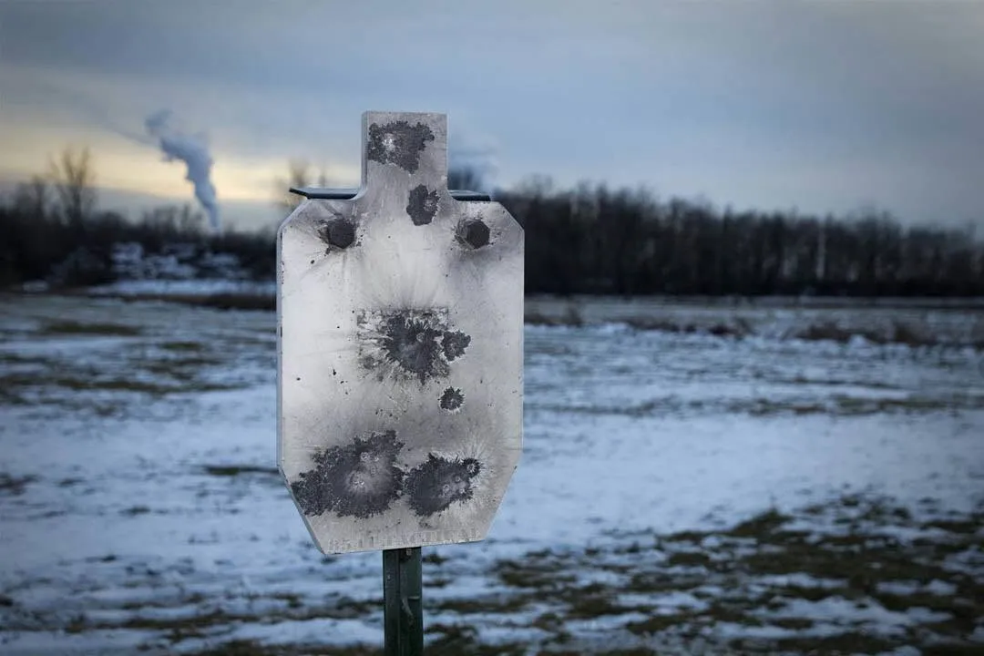 Steel silhouette target marked with bullet impacts in a snowy field