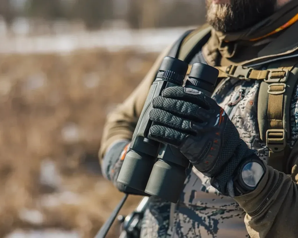 Gloved hands holding a pair of rangefinding binoculars