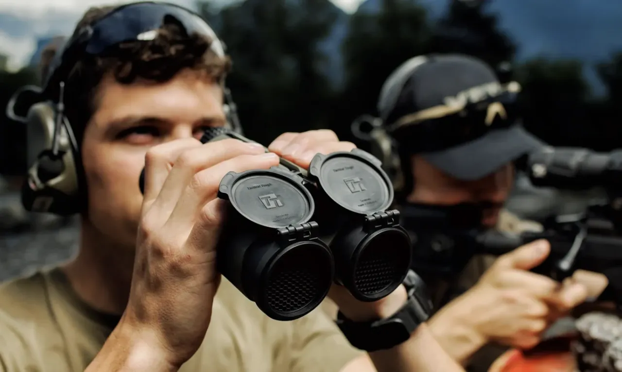 Shooters looking through rangefinding binoculars beside a rifle