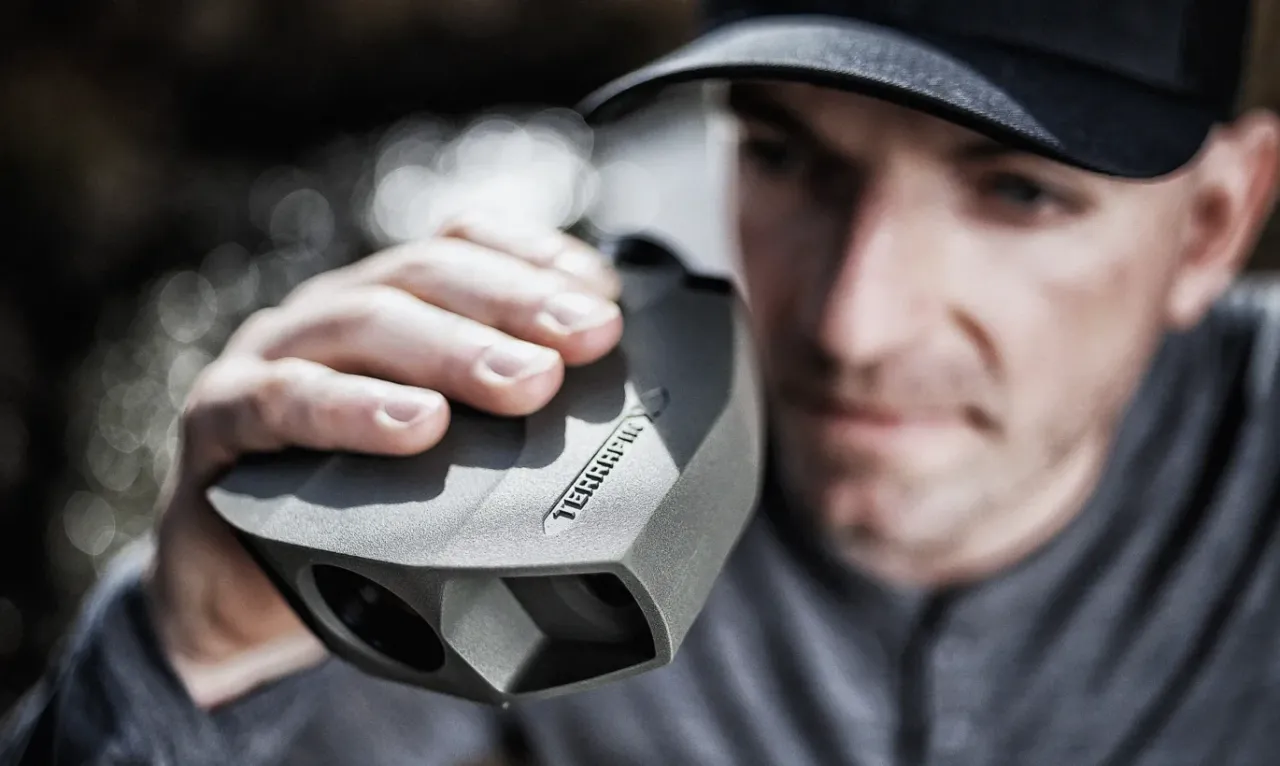 Man holding a compact laser rangefinder up to his eye